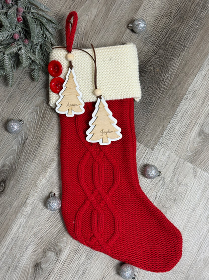Personalized wooden Christmas stocking tags with engraved names hanging on a red knit stocking